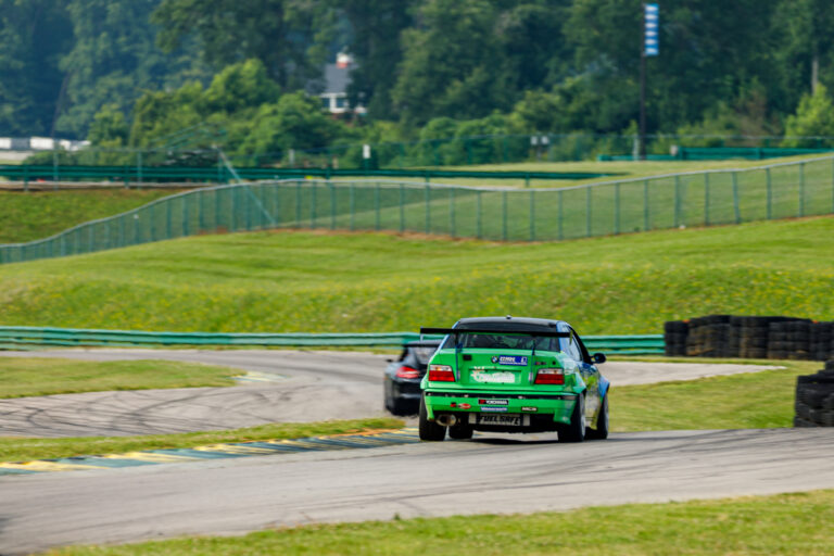the back of a green car racing at VIR with green rolling hills in the background