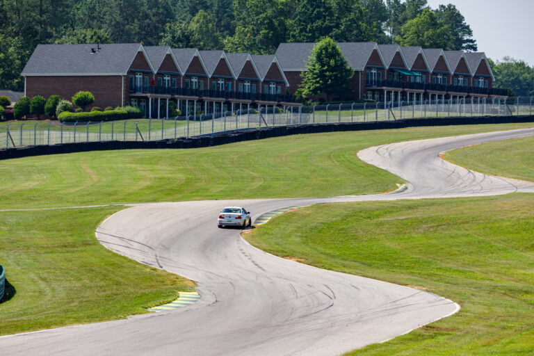 A car in the distance on the VIR track and red buildings that look like barns in the background