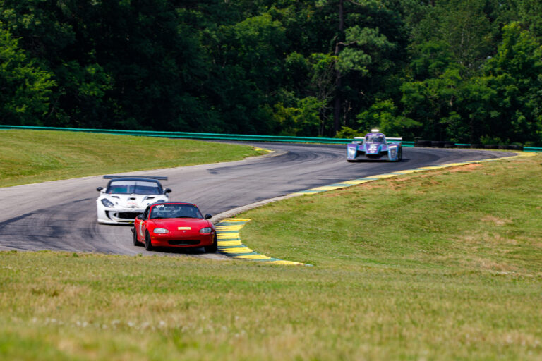 a line of 3 cars coming down a slight hill on the VIR track with trees in the background
