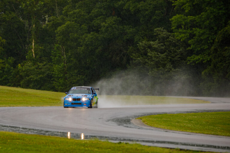 Small blue car on VIR track with exhaust behind